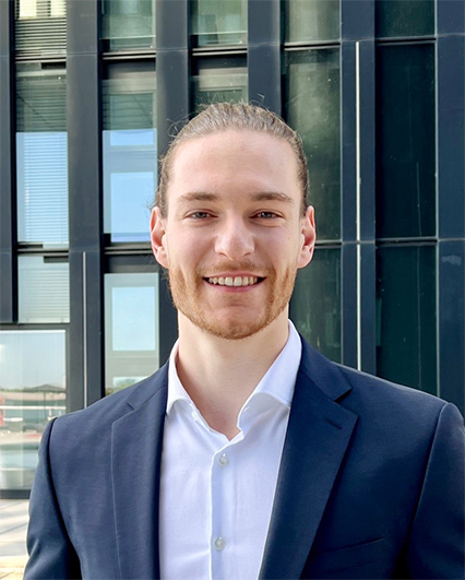 Stefan Netsome im dunkelblauen Anzug und weißem Hemd lächelt vor moderner Glasfassade.